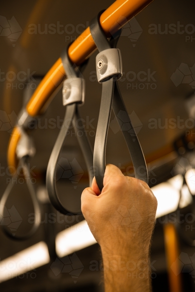 close up of mans hand holding onto a hand grip strap inside a commuter train - Australian Stock Image