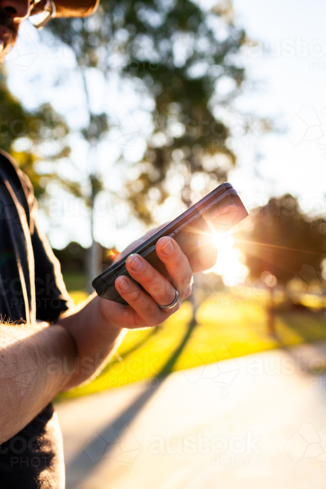 Close up of mans hands holding phone scrolling through media outdoors - Australian Stock Image