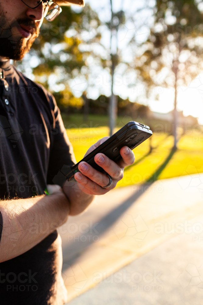 Close up of mans hands holding phone scrolling through media outdoors - Australian Stock Image