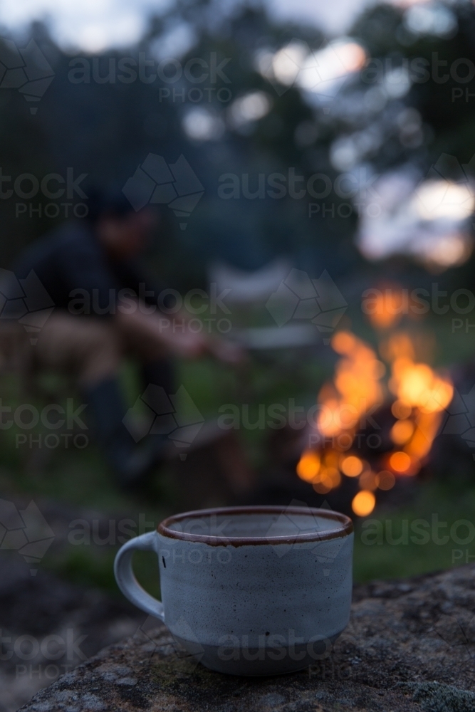 Close up of mug with man tending to fire in background on rural property - Australian Stock Image