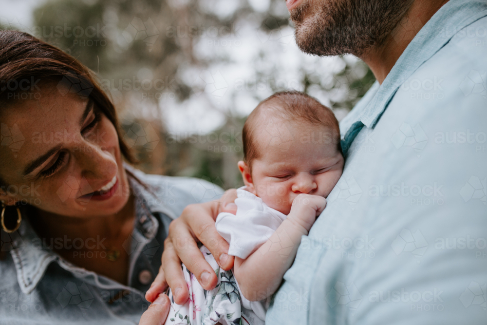 Close-up of newborn baby girl sleeping on father's chest with mother watching - Australian Stock Image