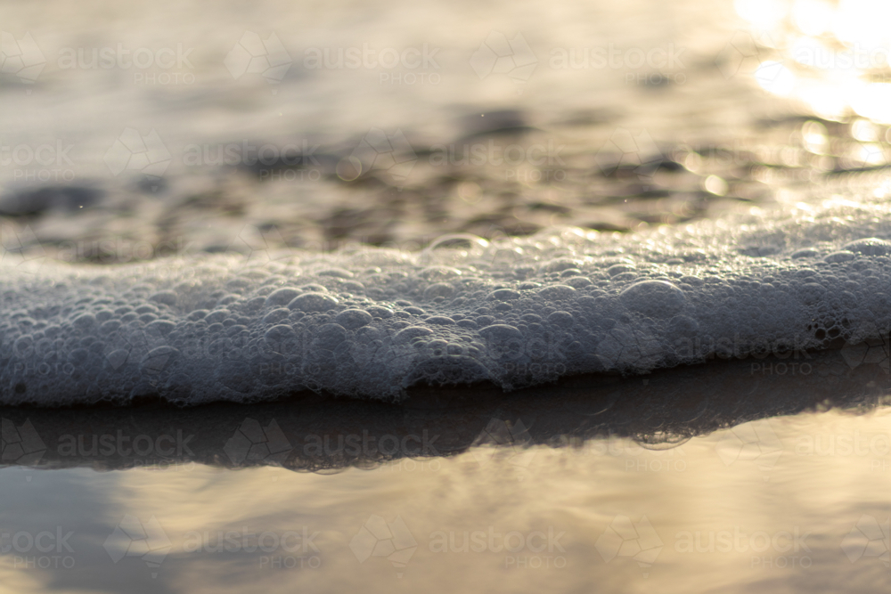 Close up of ocean water with sea foam washing up on wet sand - Australian Stock Image