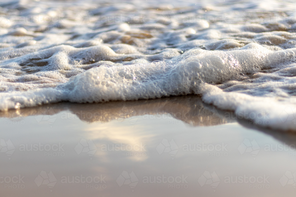 Close up of ocean water with sea foam washing up on wet sand - Australian Stock Image