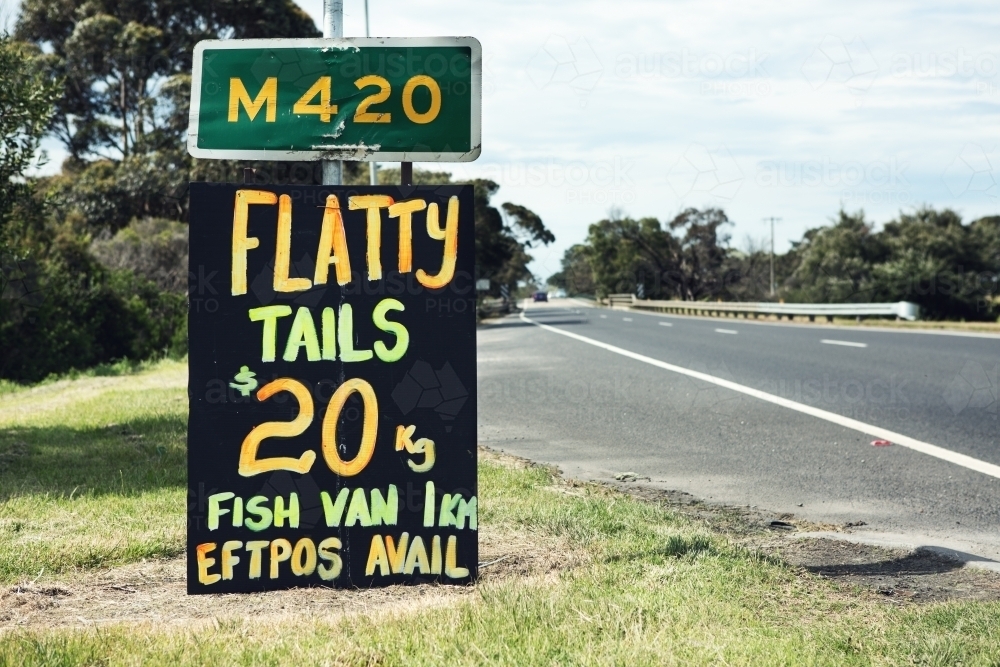 Close up of orange and yellow roadside sign advertising flathead tails - Australian Stock Image