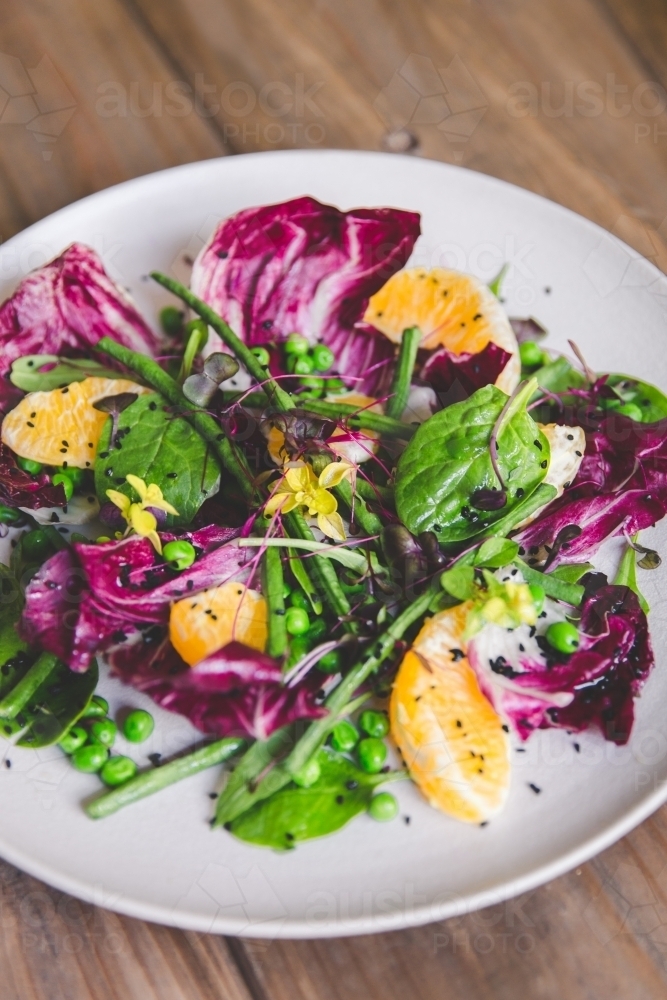 Low angle close up of naturally lit, fresh, colourful vegetable salad on timber table - Australian Stock Image