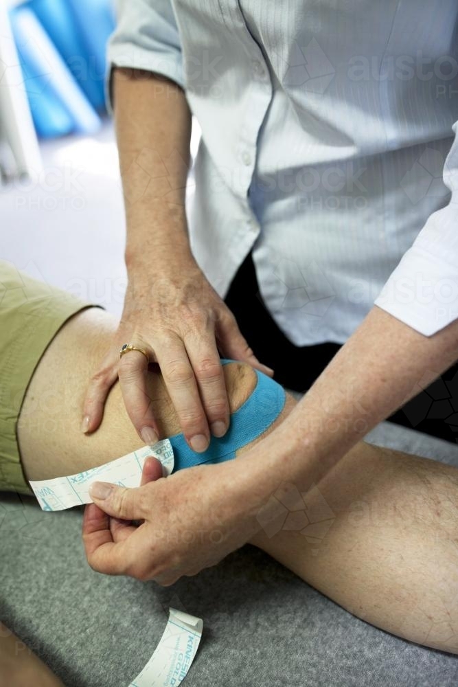 Close up of physiotherapist taping patient's knee - Australian Stock Image