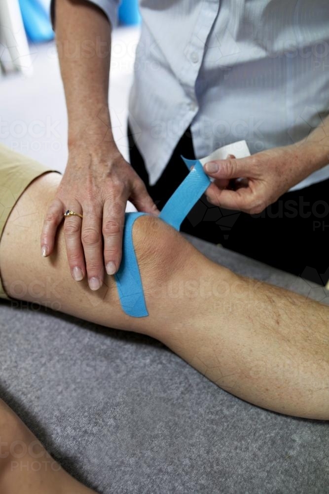 Close up of physiotherapist taping patient's knee - Australian Stock Image