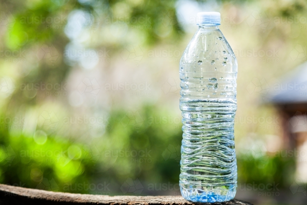 Close up of plastic water bottle outside with green bokeh background - Australian Stock Image