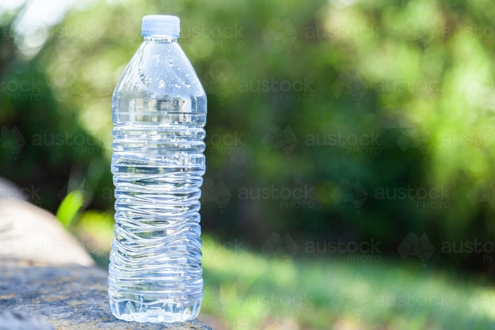 Close up of plastic water bottle outside with green bokeh background - Australian Stock Image