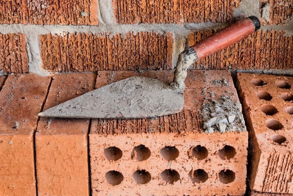 Close-up of rugged brick wall with loose bricks & trowel on building site - Australian Stock Image