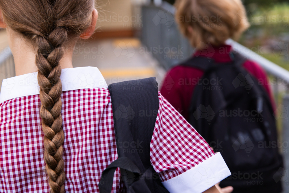 close up of school girl with a backpack on her shoulder and long hair in a plait down her back - Australian Stock Image