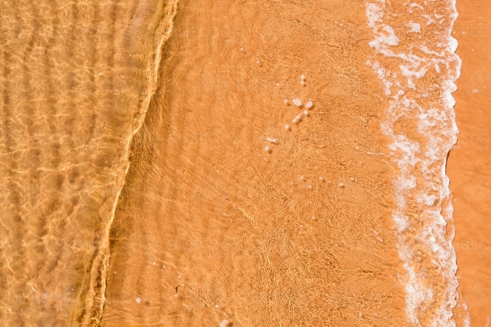 Close up of small wave over rippled sand - Australian Stock Image