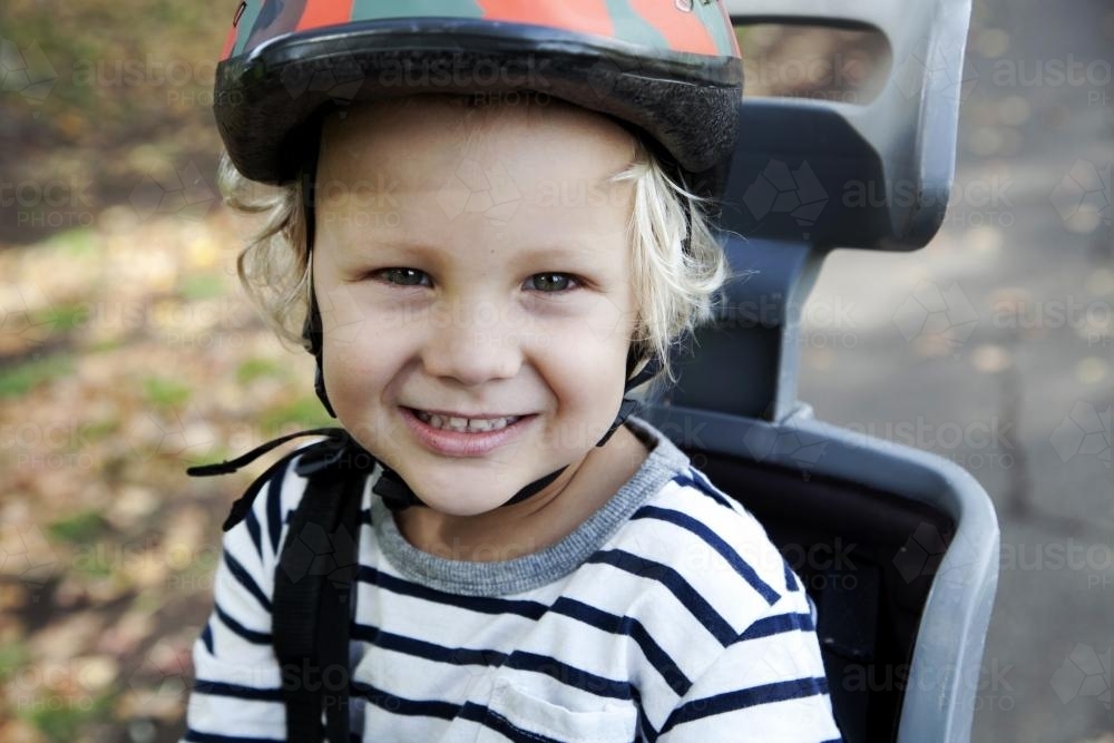 Close up of smiling boy wearing helmet in bike seat - Australian Stock Image