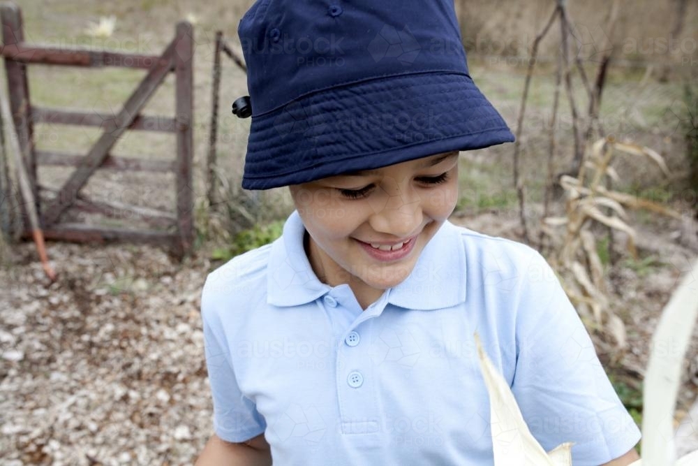 Close up of smiling boy wearing school uniform and hat outside - Australian Stock Image