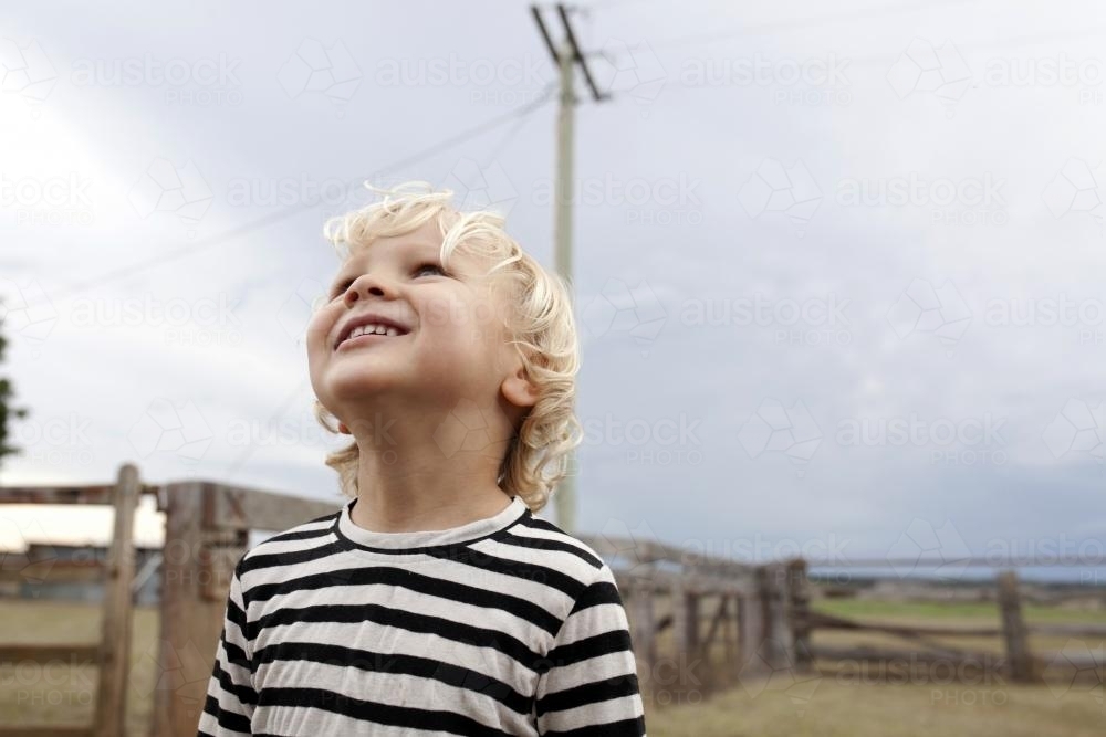 Close up of smiling young boy looking up at sky - Australian Stock Image