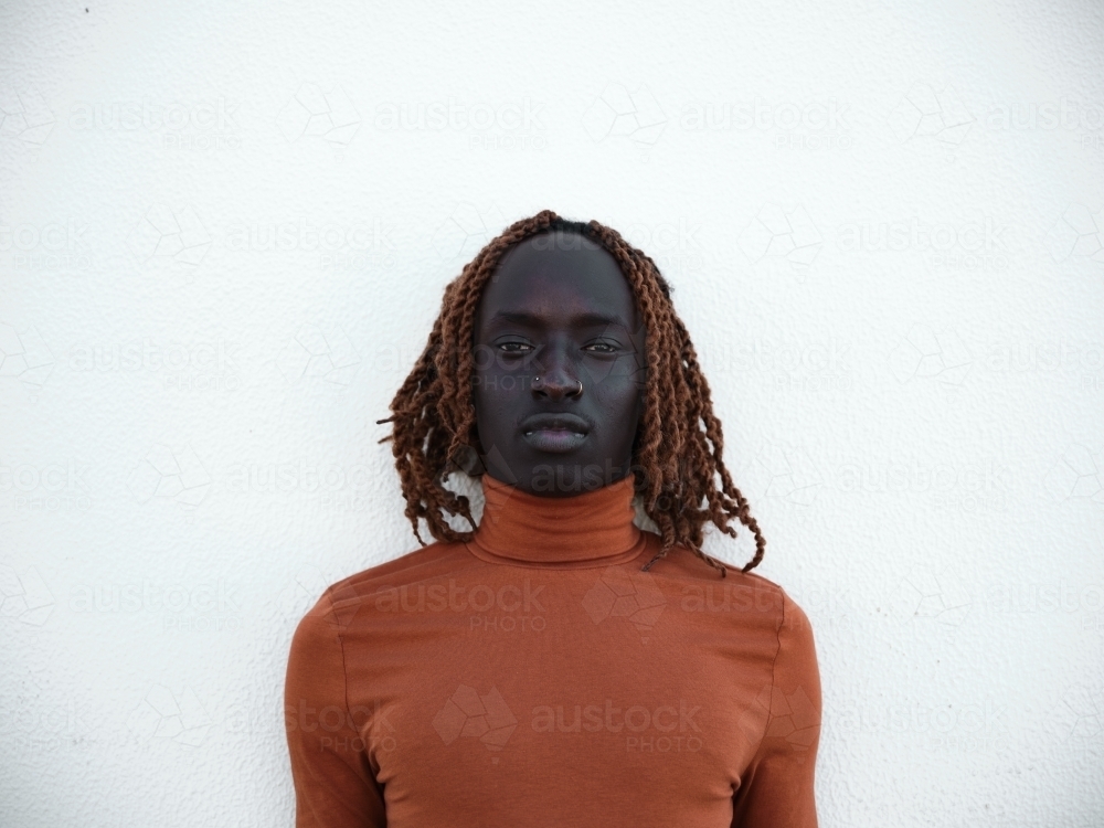 Close-up of South Sudanese man wearing orange turtleneck in front of a blank wall - Australian Stock Image