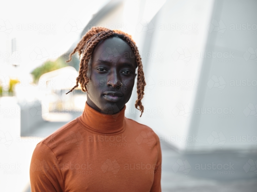 Close-up of South Sudanese man wearing orange turtleneck with urban background - Australian Stock Image