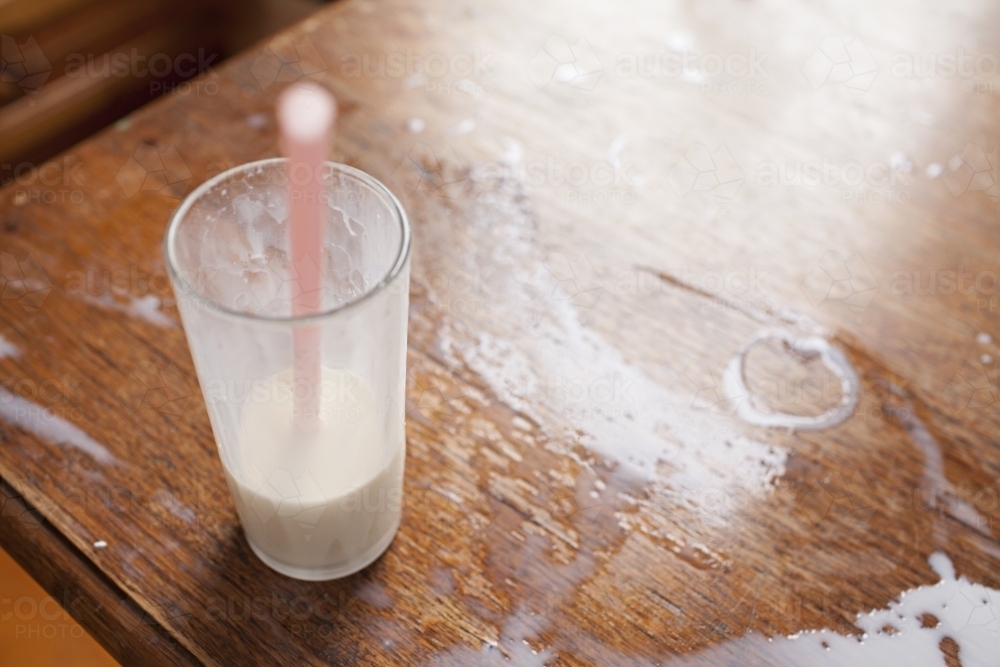Close up of spilt milk on wooden table top - Australian Stock Image