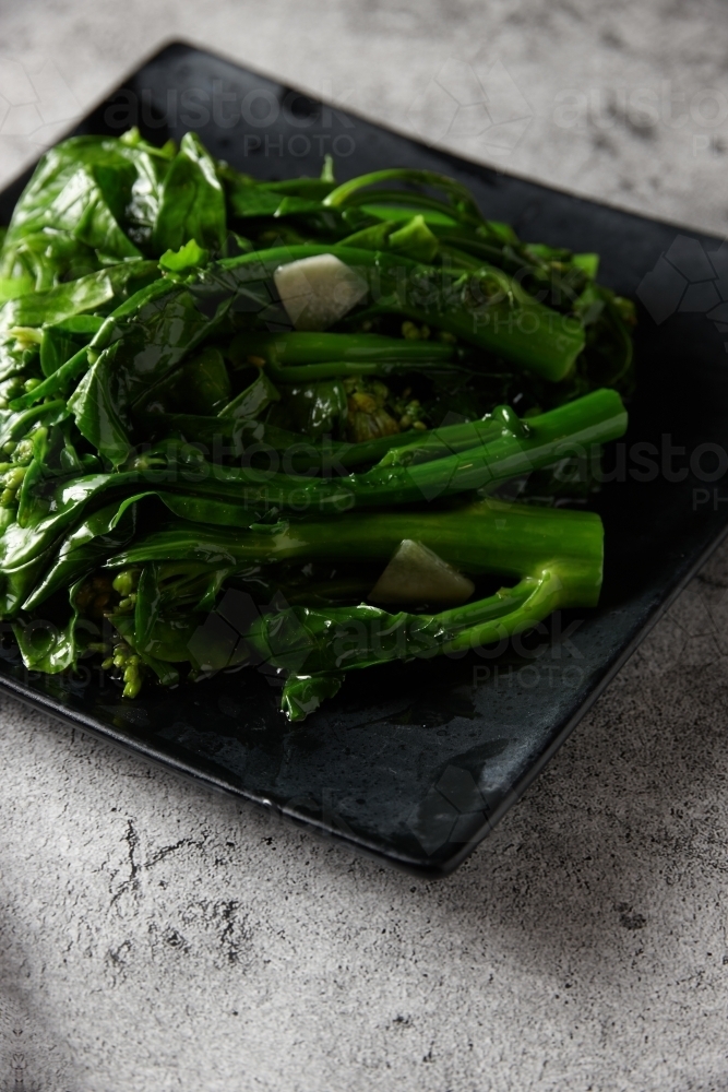 Close up of steamed green vegetables on black plate - Australian Stock Image