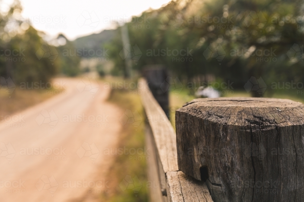 Close up of timber post of rural property fence, on side of winding dirt road - Australian Stock Image