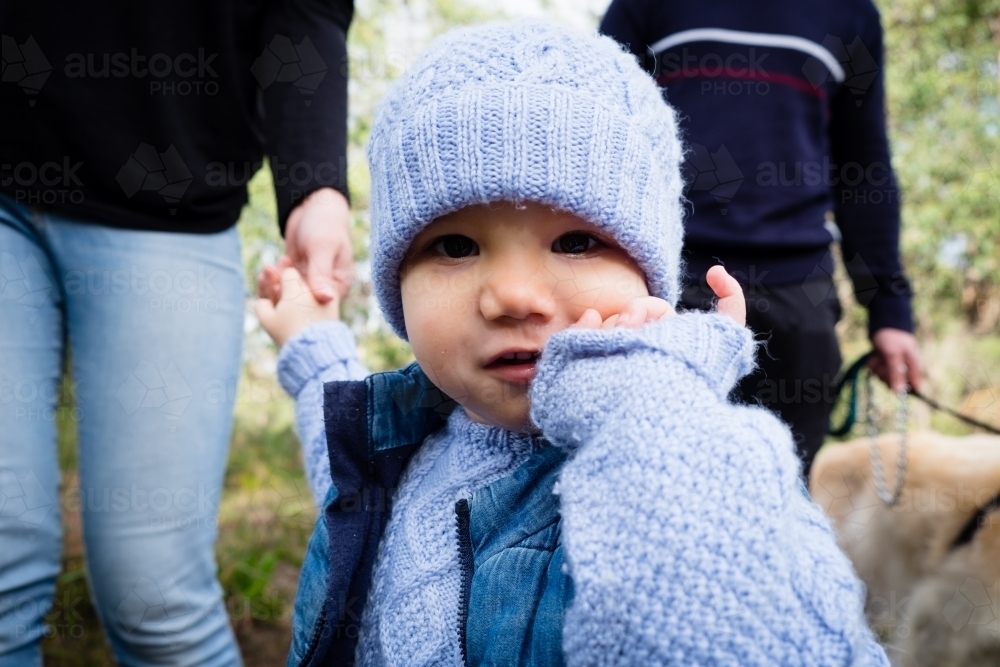 Close up of Toddler in beanie looking at camera inquisitively with parents in background - Australian Stock Image