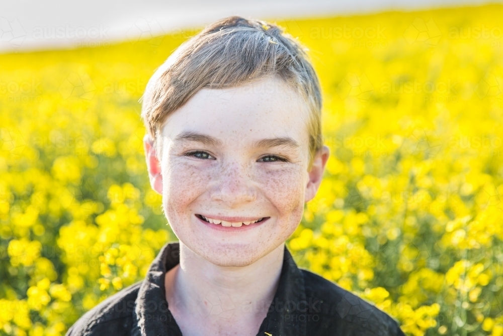 Close up of tween boy smiling on farm with canola field - Australian Stock Image