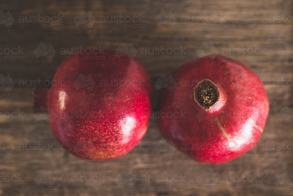 Close up of two red pomegranates with a wooden background - Australian Stock Image