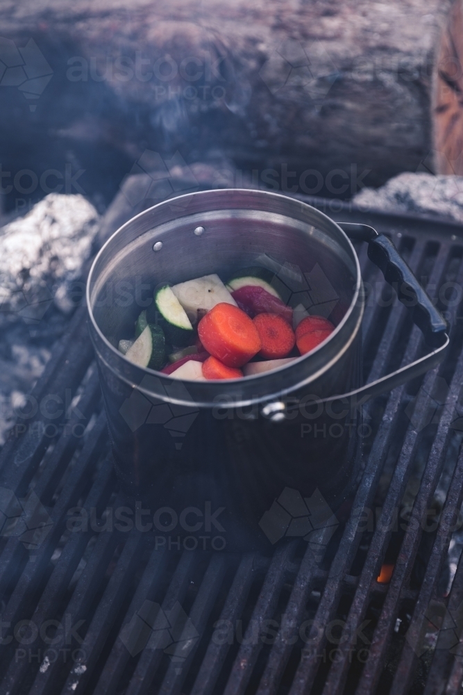 Close up of vegetables cooking in steel pot on the grill on a smoking campfire - Australian Stock Image