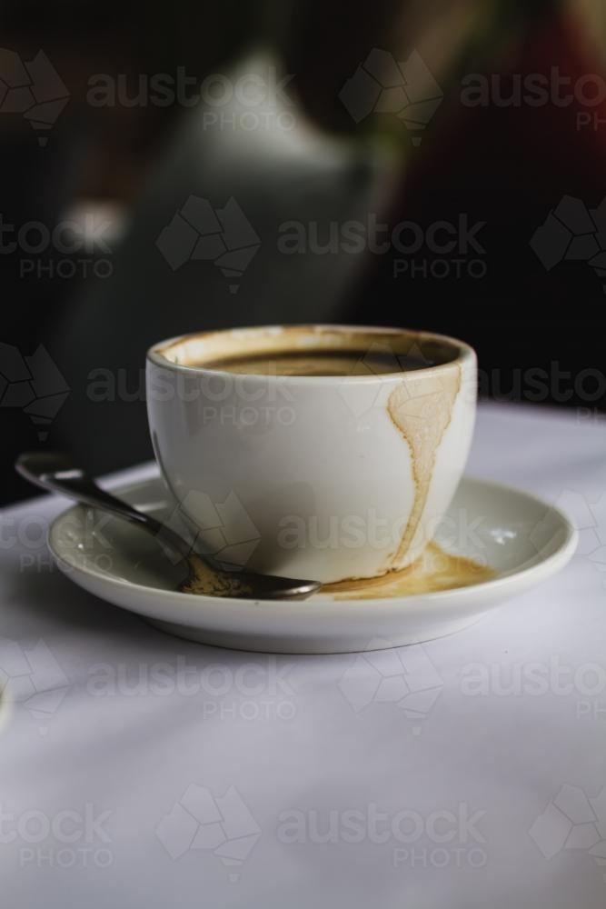 Close up of white espresso short black coffee spilt on saucer on white tablecloth - Australian Stock Image