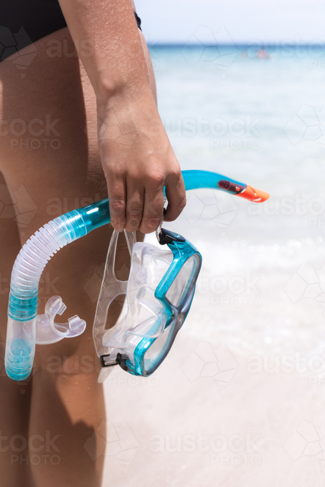 Close up of woman holding snorkel in hand at clear blue beach - Australian Stock Image