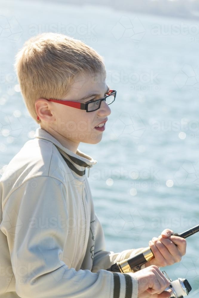 Close up of young boy fishing off wharf - Australian Stock Image