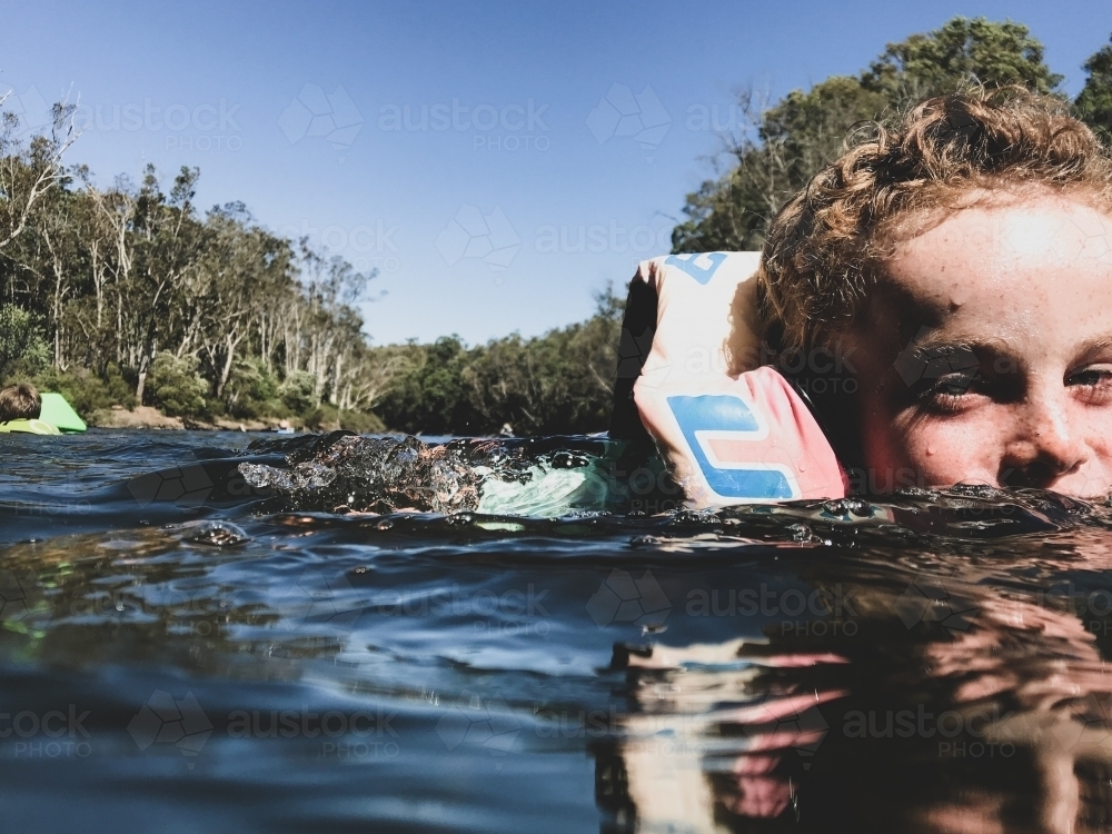 Close up of young boy swimming in river wearing personal flotation device - Australian Stock Image
