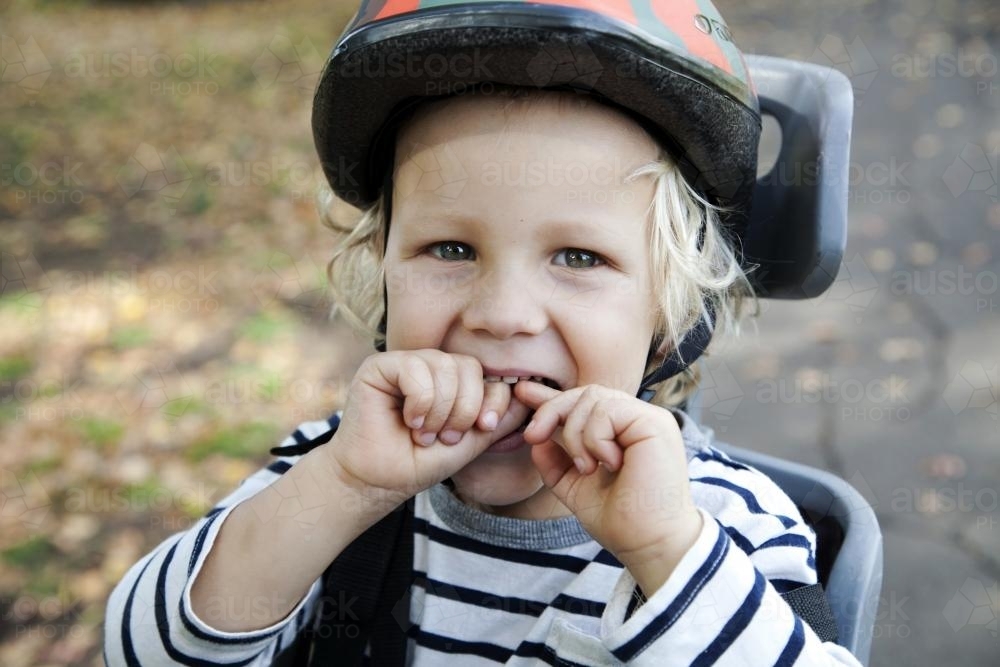 Close up of young boy wearing helmet in bike seat laughing - Australian Stock Image
