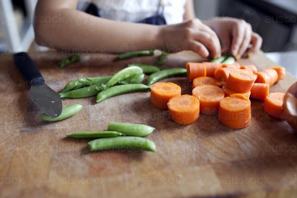 Close up of young child helping chop vegetables - Australian Stock Image