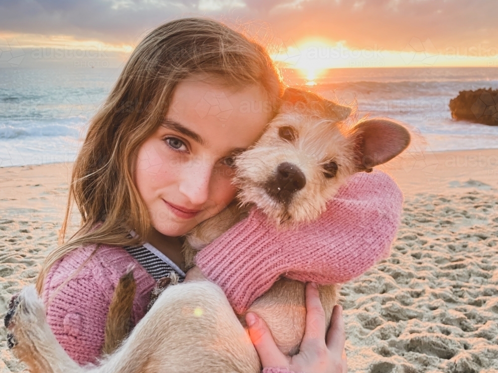 Close up of young girl cuddling puppy on the beach at sunset with ocean in background - Australian Stock Image