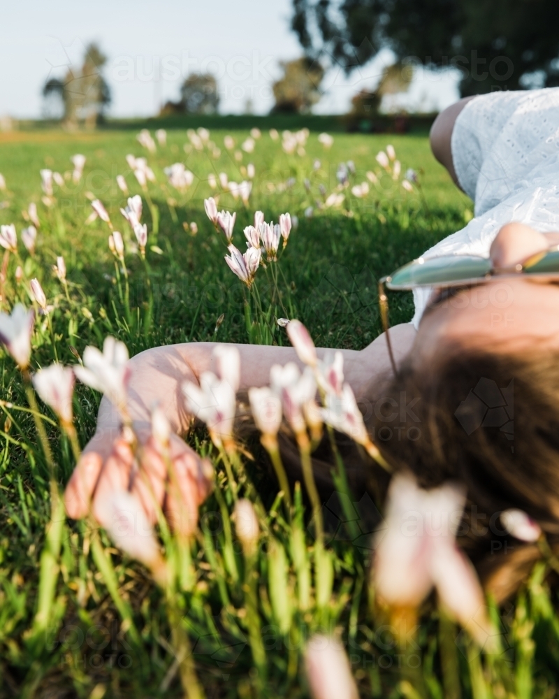 Close up of young girl lying on her back in a field of flowers - Australian Stock Image