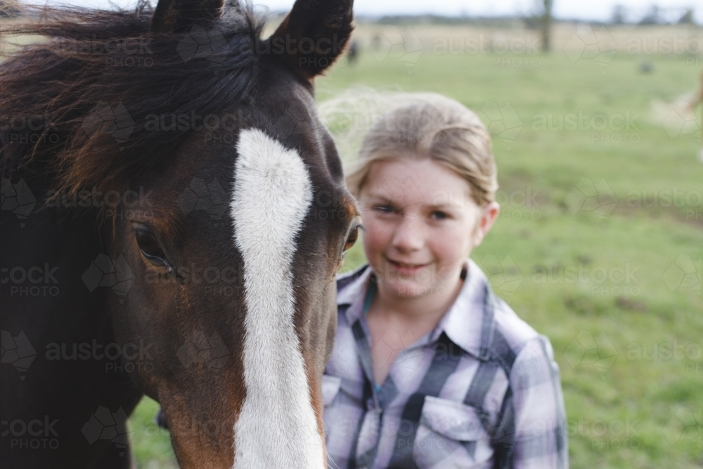 Close up of young girl standing beside horse in paddock - Australian Stock Image