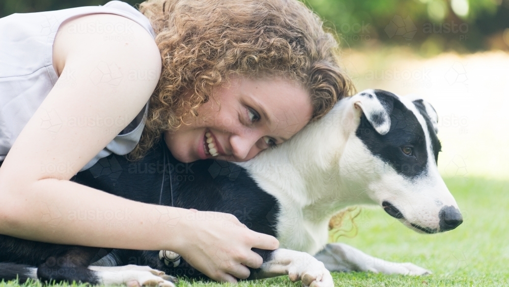 Close up of young girl with her dog laying on grass - Australian Stock Image