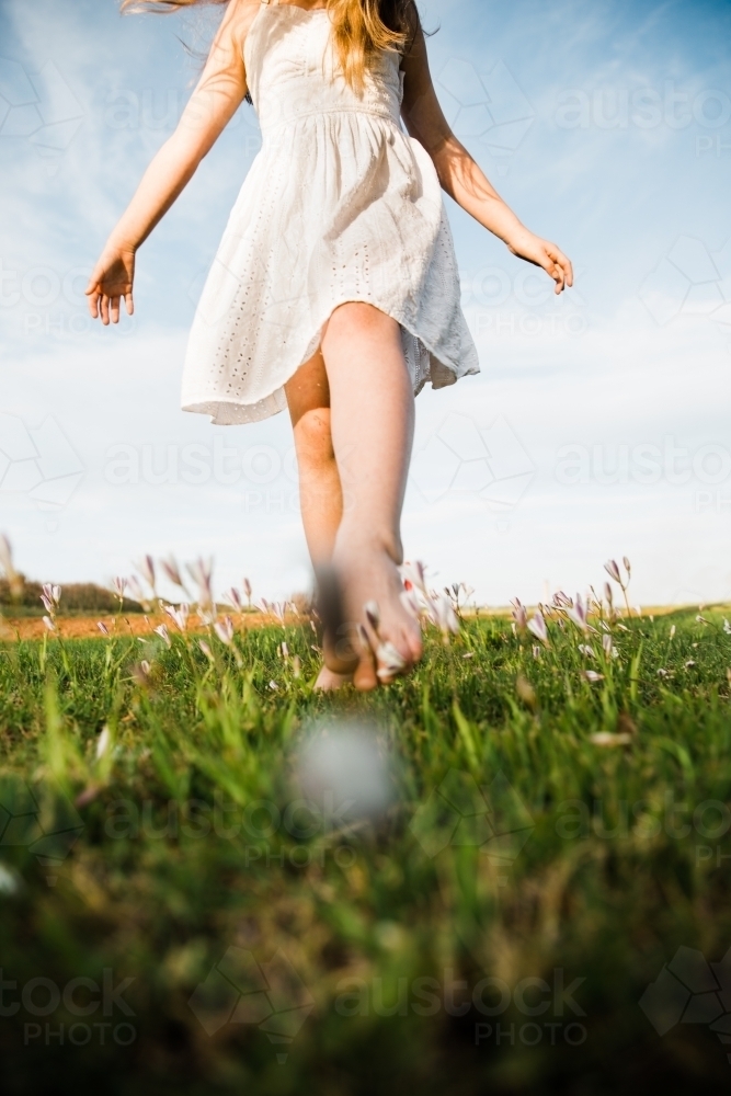 Close up of young girls legs walking in a field of flowers - Australian Stock Image