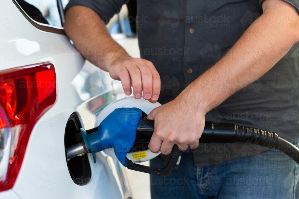 Close up of young man filling car with petrol at service station - Australian Stock Image