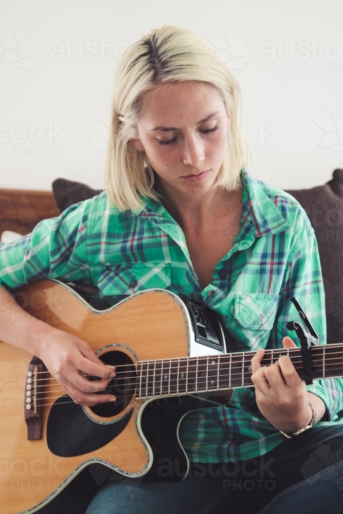 Close up of young woman looking down as she plays the guitar on her bed - Australian Stock Image
