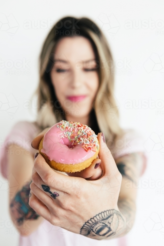 Close up on an iced pink donut being held to camera by a girl - Australian Stock Image