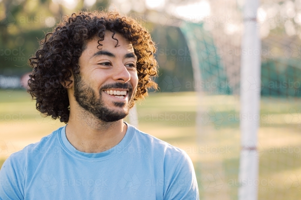 Close up photo of a smiling man with curly hair with beard wearing blue shirt on a sunny day - Australian Stock Image