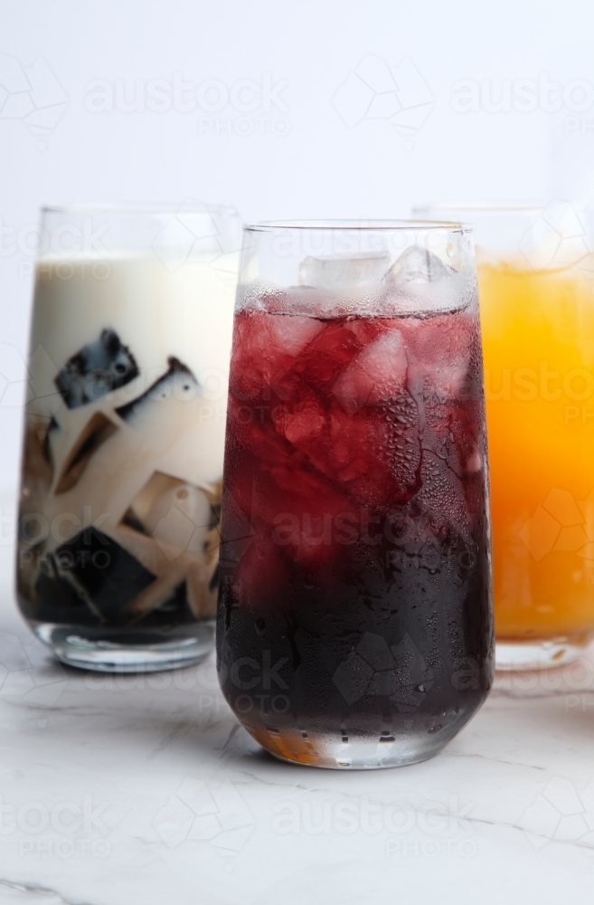 Close-up photo of colorful refreshing juices in a tall glass served on a white marble countertop - Australian Stock Image