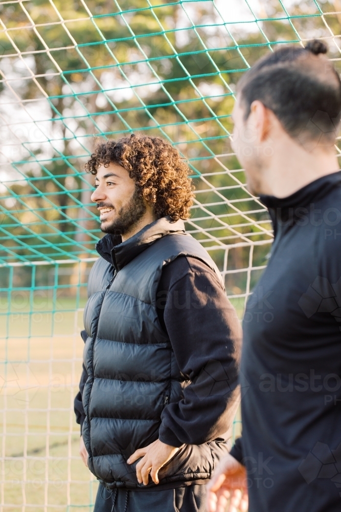 Close up photo of two interracial young men standing on the field near the net smiling - Australian Stock Image