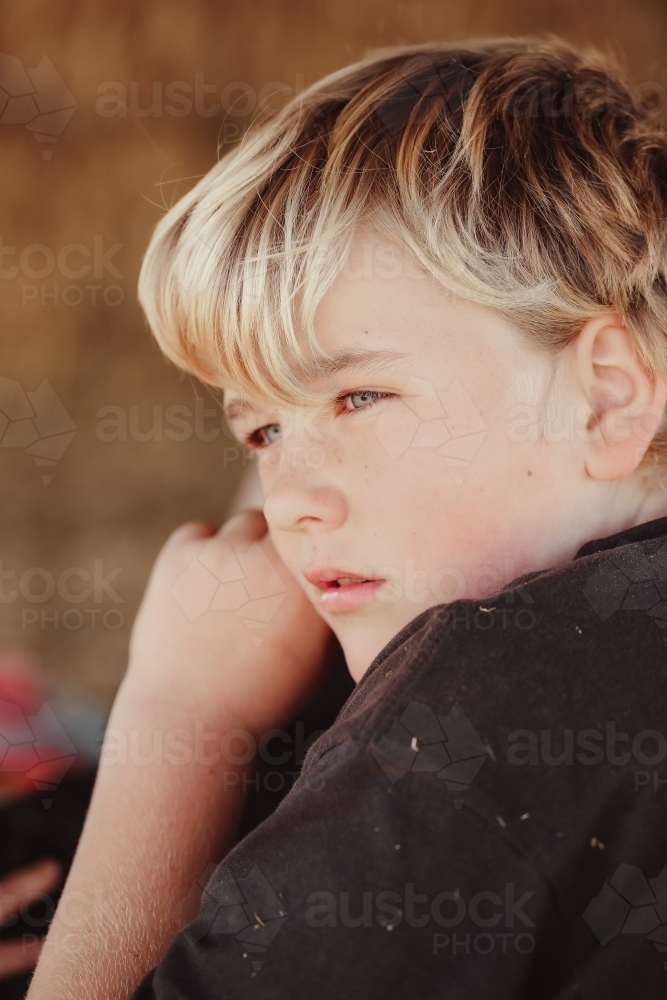 Close up portrait image of young blond boy with blue eyes. Farm kid in moment of reflection - Australian Stock Image