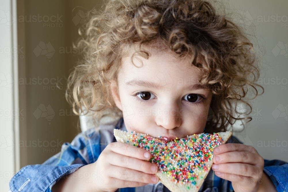 Close up portrait of a young boy with blond curly hair eating a slice of fairy bread - Australian Stock Image