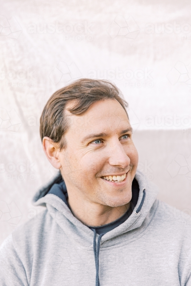 Close-up portrait of a young sportsman smiling while looking at the side wearing a grey hoodie - Australian Stock Image