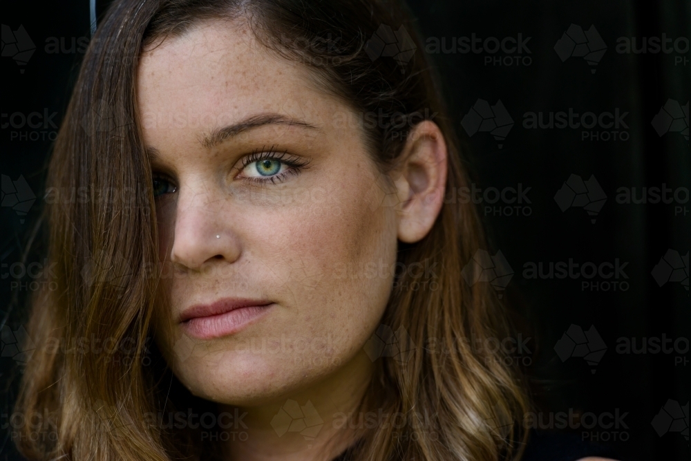 Close up portrait of a young woman with long hair covering one eye - Australian Stock Image