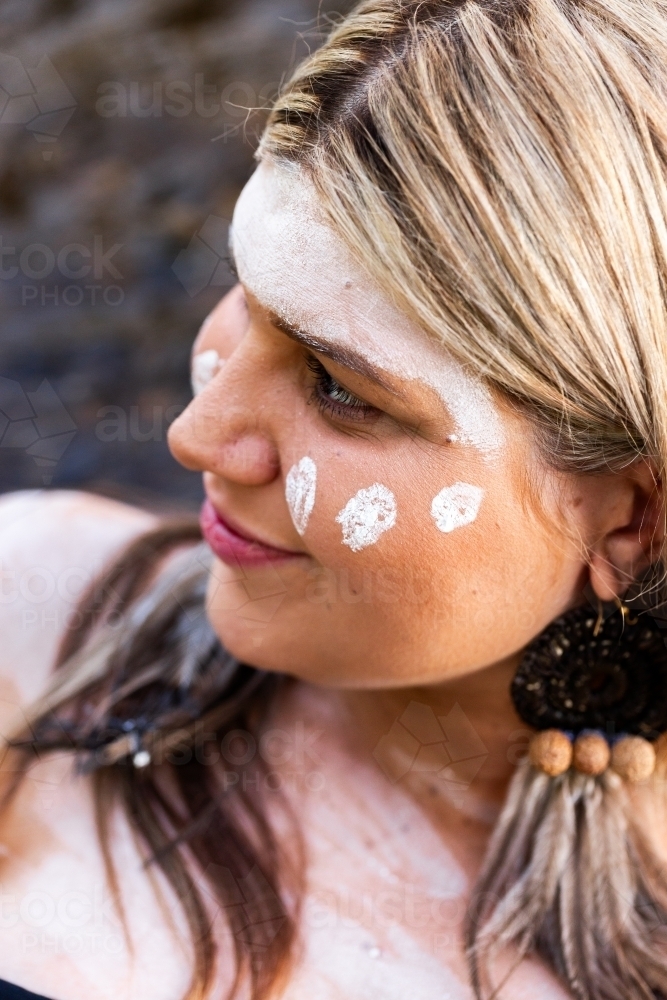Close up portrait of aboriginal woman with woven earring and ochre paint on face - Australian Stock Image